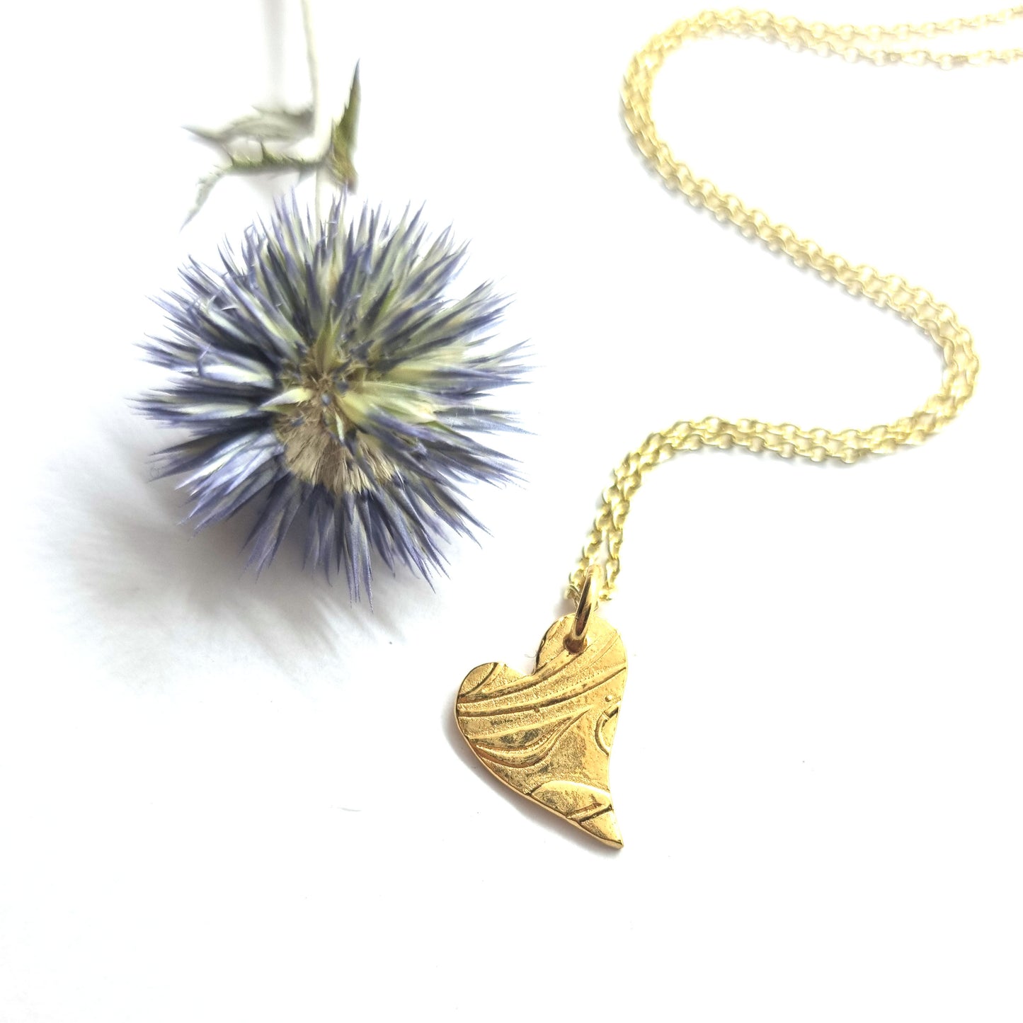 Yellow gold vermeil asymmetrical heart pendant with a leaf & vine design on a yellow gold vermeil chain. Pictured with a flower.