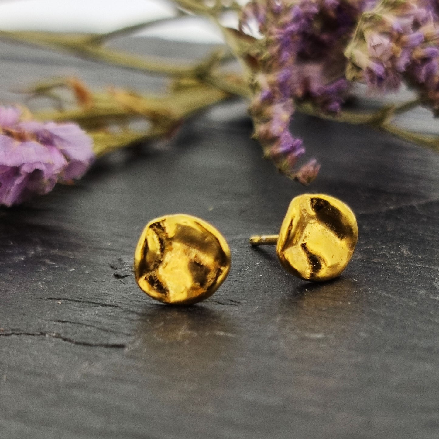 Yellow gold vermeil round stud earrings with a crumpled textured surface. Pictured with purple flowers.
