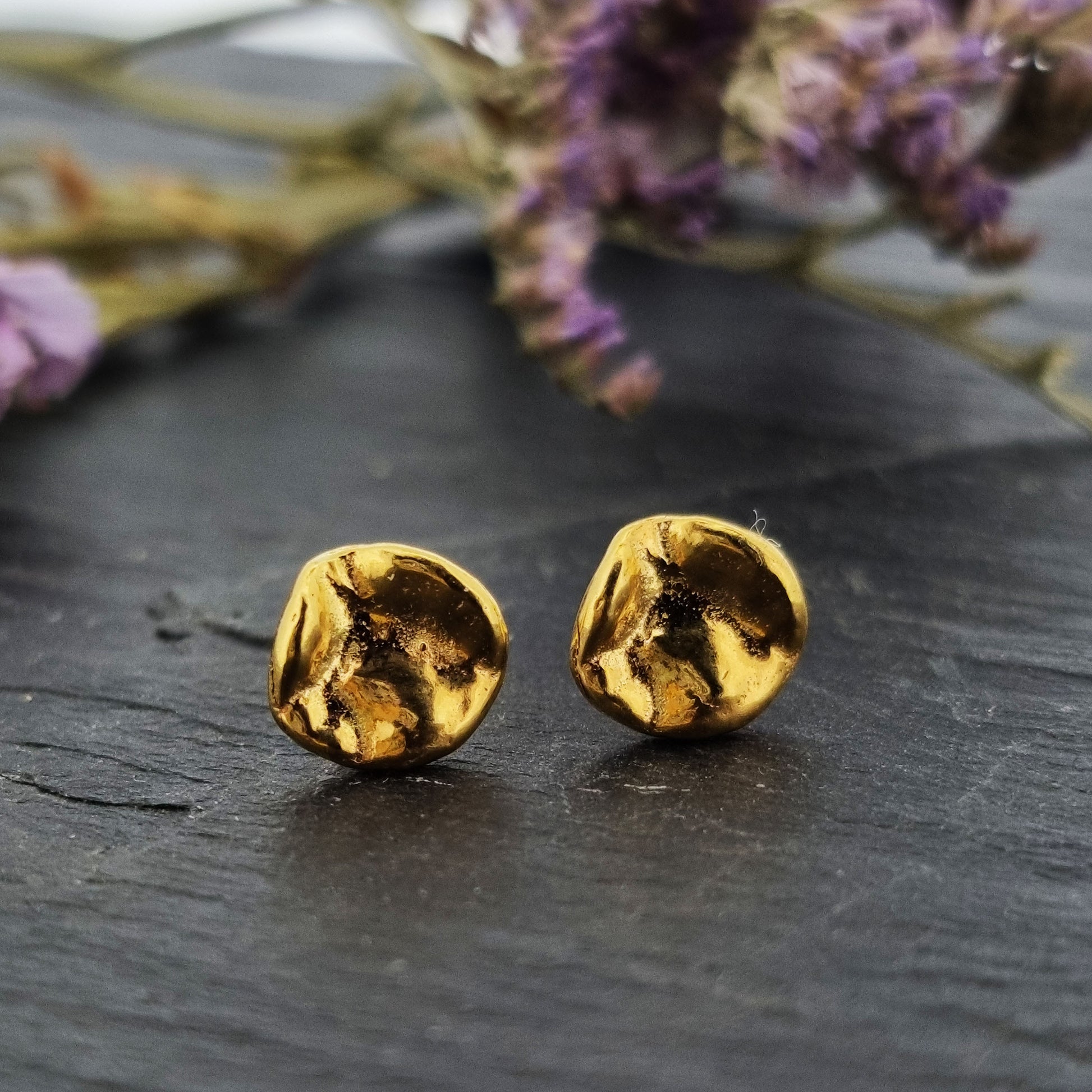 Yellow gold vermeil round stud earrings with a crumpled textured surface. Pictured with purple flowers.