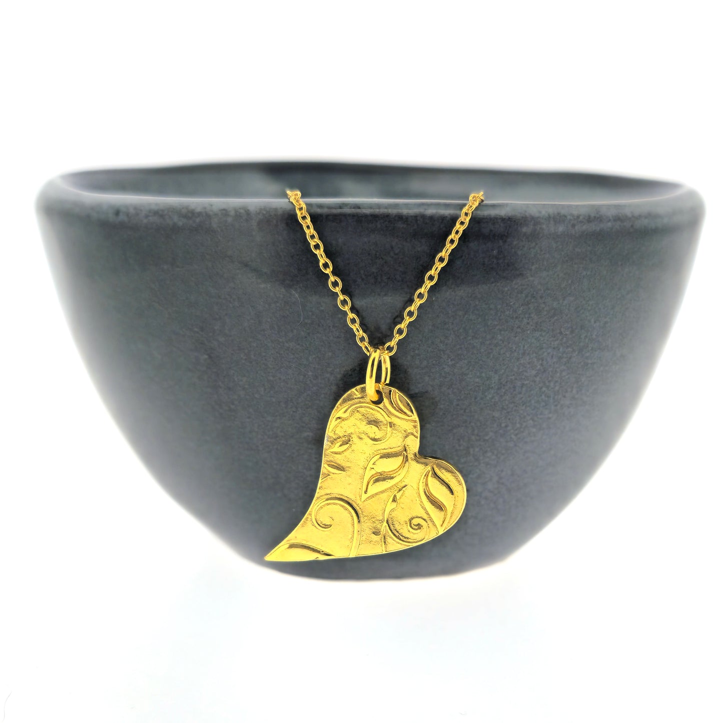 Yellow gold vermeil asymmetrical heart pendant with a leaf & vine design on a yellow gold vermeil chain. Large. Shown on a black bowl.