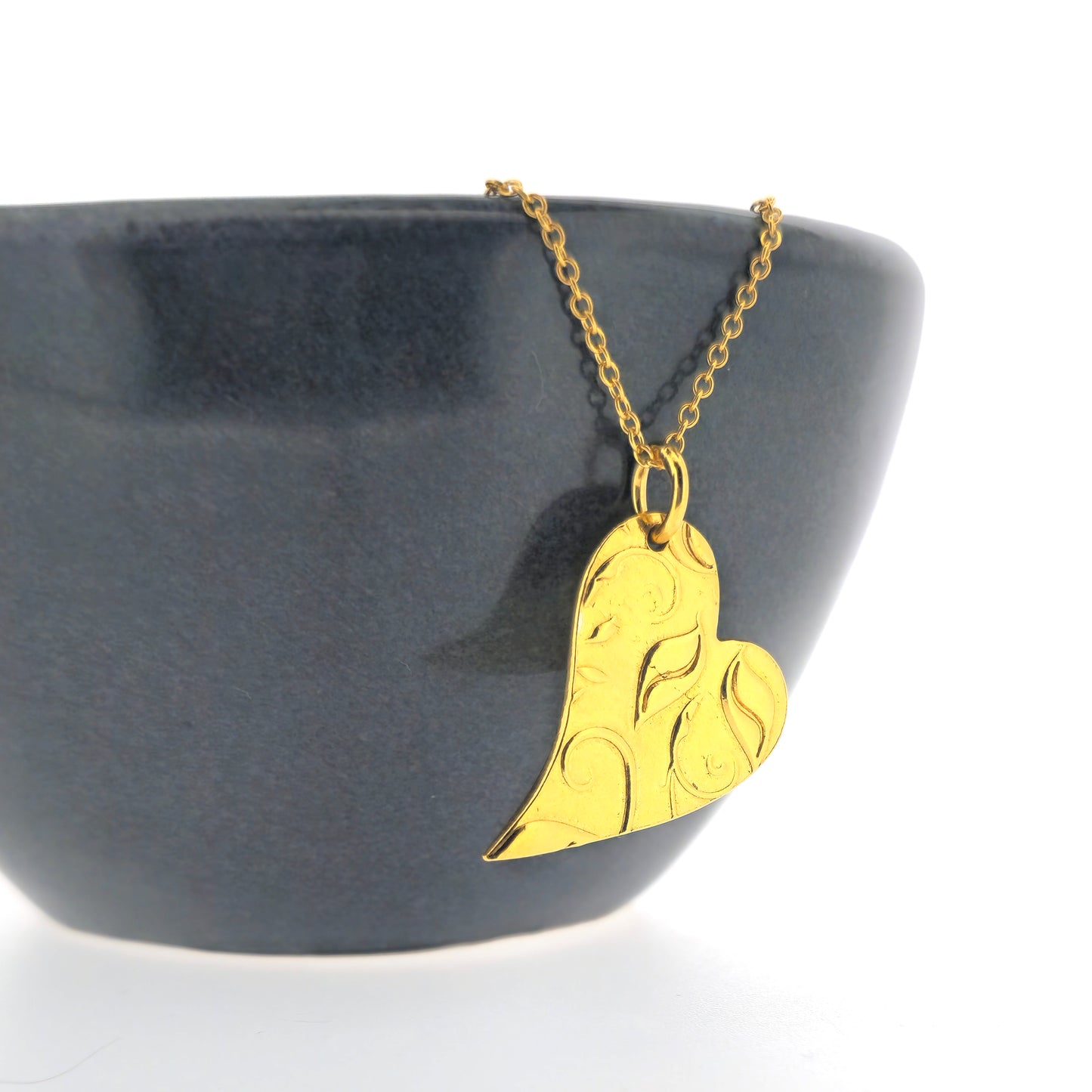 Yellow gold vermeil asymmetrical heart pendant with a leaf & vine design on a yellow gold vermeil chain. Large. Shown on a black bowl.