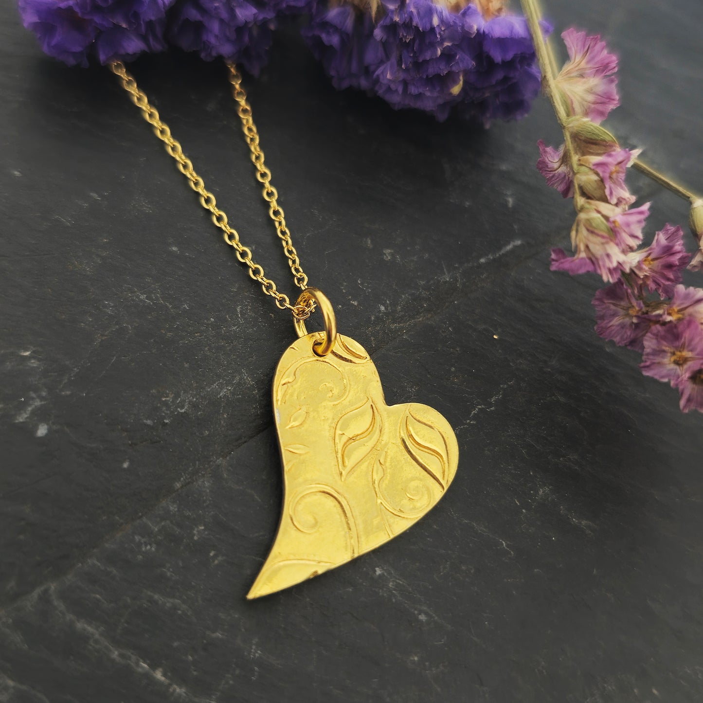 Yellow gold vermeil asymmetrical heart pendant with a leaf & vine design on a yellow gold vermeil chain. Large. Shown on slate with flowers.