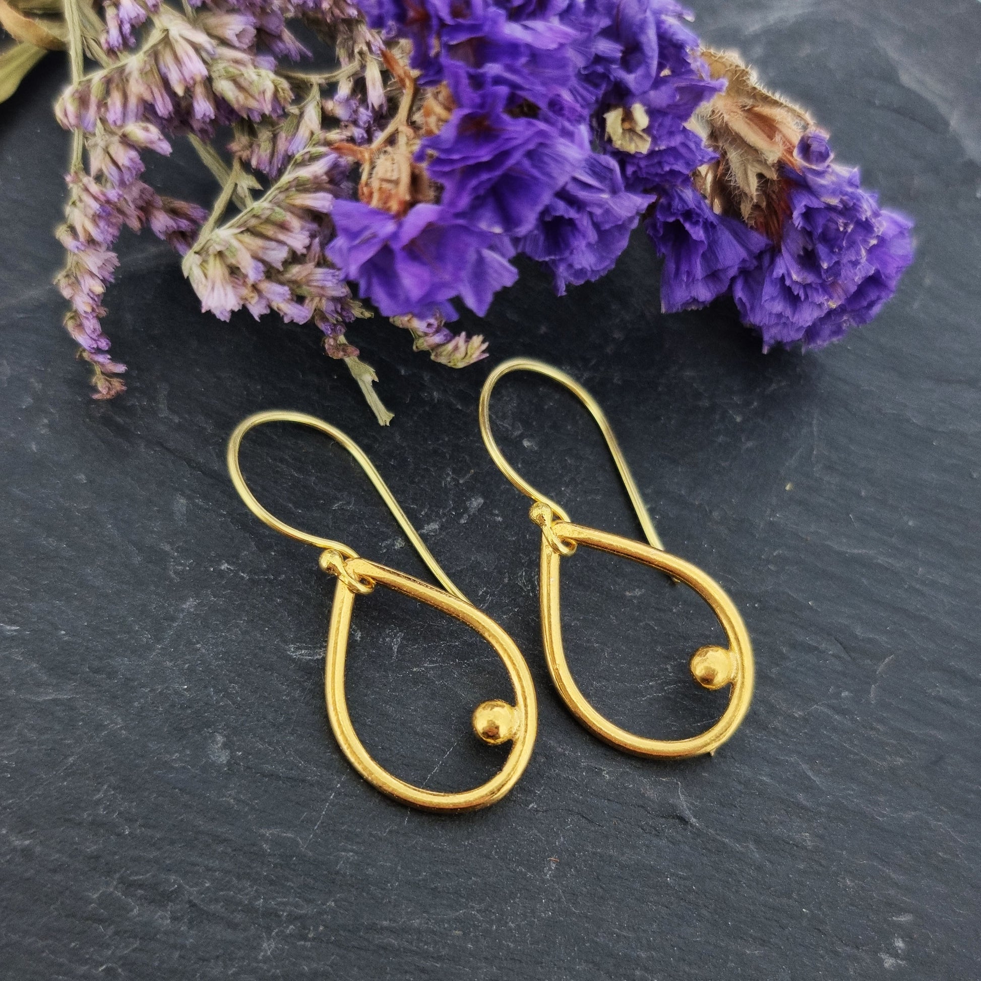 Yellow gold vermeil open teardrop with off-center ball drop earrings. Pictured with flowers.