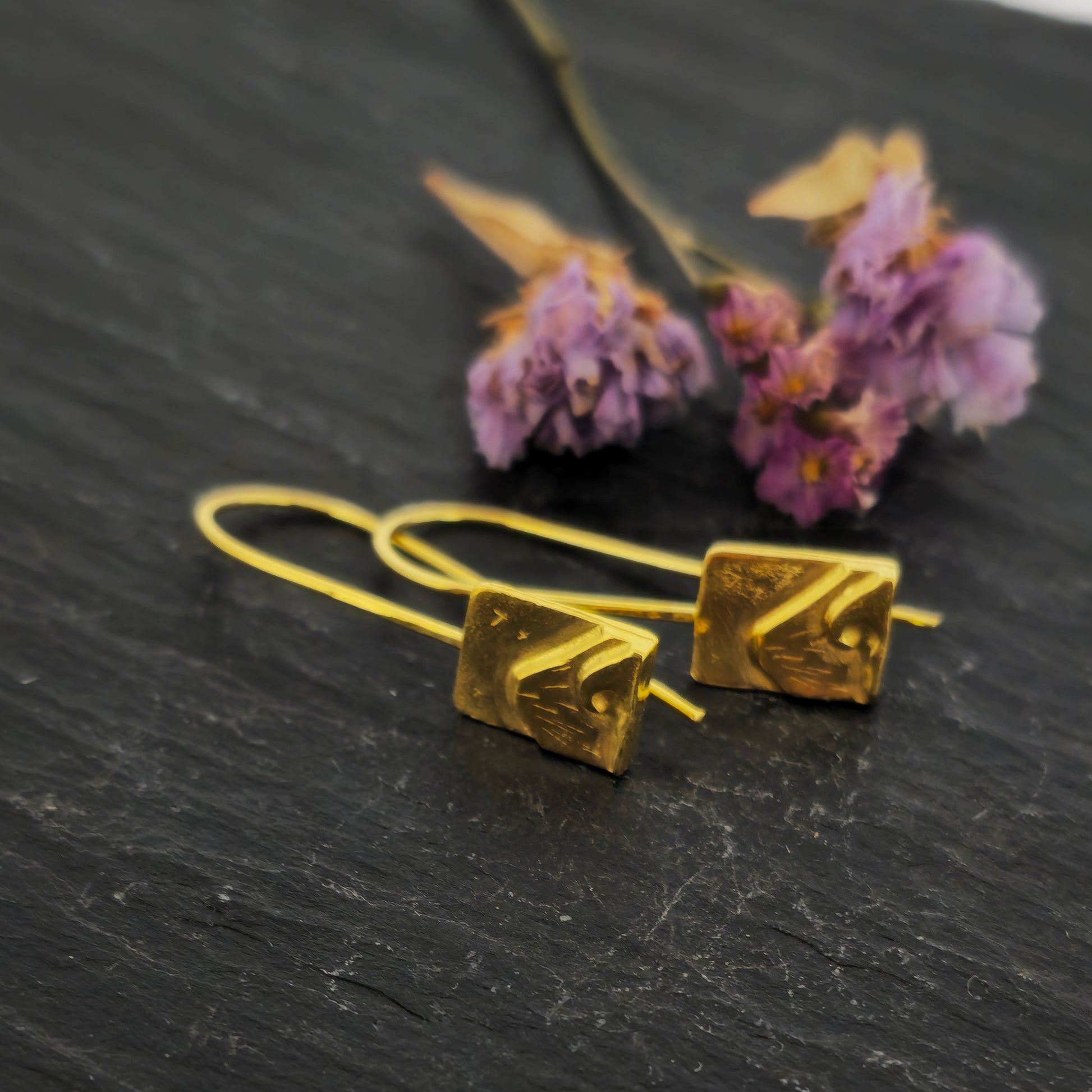 Yellow gold vermeil drop earrings featuring a rectangular section with a mountain and wave scene on ear wires. Pictured on slate with flowers.