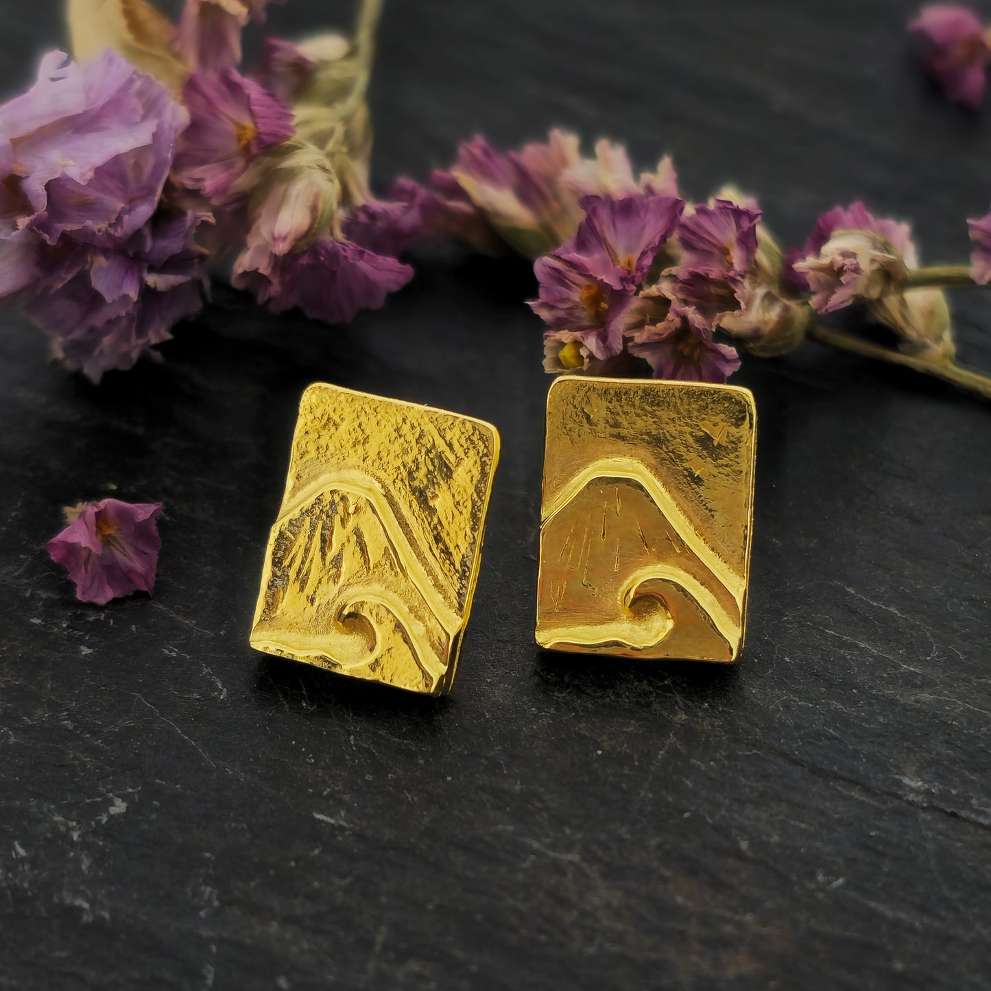 Yellow gold vermeil rectangle stud earrings featuring a mountain and sea scene. Pictured on slate with flowers.