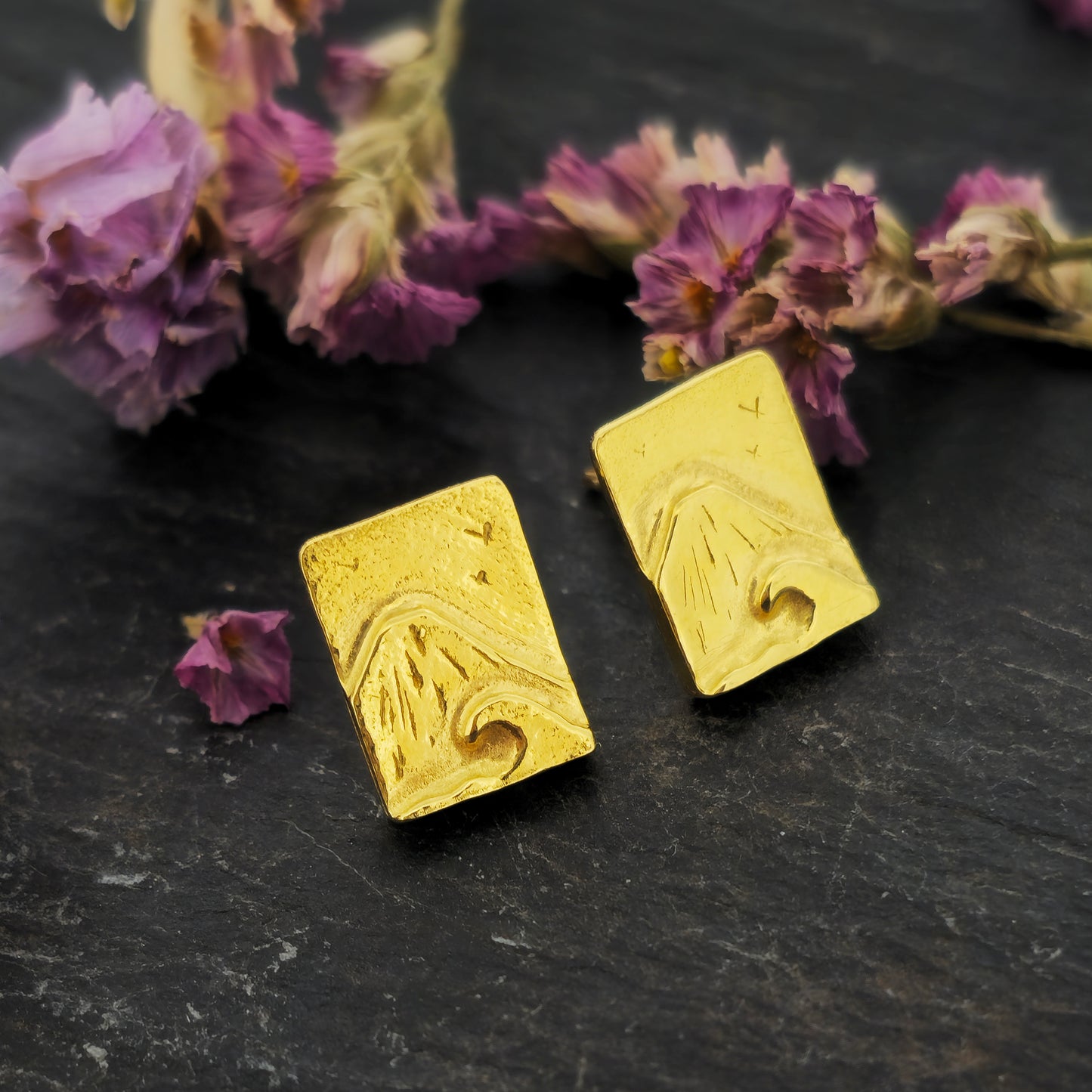 Yellow gold vermeil rectangle stud earrings featuring a mountain and sea scene. Pictured on slate with flowers.