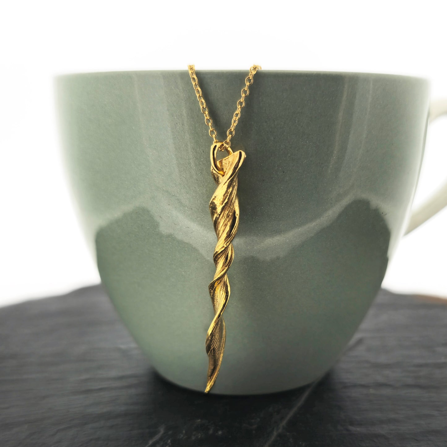 A yellow gold vermeil twist pendant suspended on a yellow gold vermeil chain. Shown on a bowl.