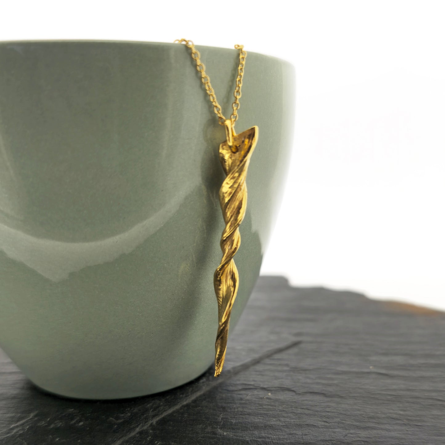 A yellow gold vermeil twist pendant suspended on a yellow gold vermeil chain. Shown on a bowl.